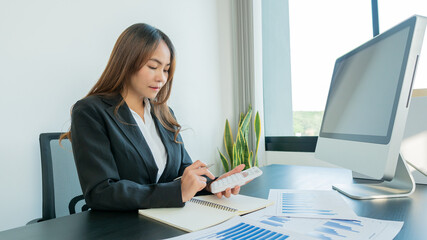 A confident young businessman analyzes graph data and calculates with a calculator and uses a computer while in the office.