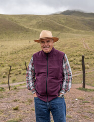 hispanic senior man with hat in a valley during a trip with mountains with clouds in the background - fresh air concept - latinx