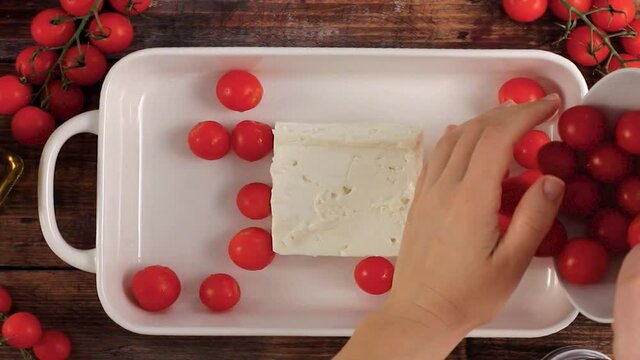 Making baked feta cheese with cherry tomatoes, herbs and olive oil, trendy food recipe