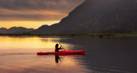 Fototapeta premium Adventure Caucasian Adult Woman Kayaking in Red Kayak surrounded by Canadian Mountain Landscape. Sunset Sky Art Render. Widgeon Valley, Pitt Meadows, Vancouver, British Columbia, Canada.