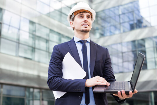 Portrait of cheerful male builder working with laptop outdoors.