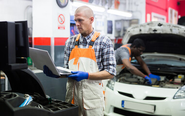 Mechanic with laptop near car engine in auto service