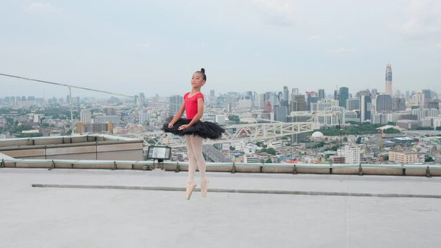 Ballet girl with red dress and black skirt dance on rooftop or terrace of high building in big city with day light and she look happy for dancing or practice the dance.