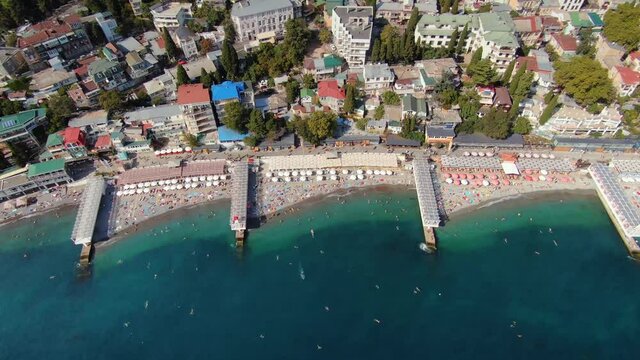 Aerial above best seaside city beach Yalta Crimea Ukrain vacation on shores of blue Black Sea. Resort cityscape from above. Many people resting sunbathing. City center embankment. Summy summer. Travel