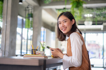 Obraz premium Beautiful asian businesswoman in the cafe, using smartphone and smiling.