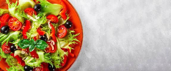  Simple summer salad of lettuce, tomatoes with olives and olive oil on a red plate and light gray background close-up, web banner with copy space for text