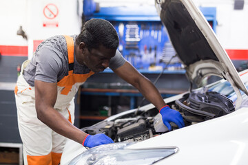 Professional american mechanic man in uniform repairing car engine in auto repair shop garage