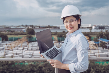 Female Civil Engineer in Safety Hard Hat Using Laptop While Control Production in Manufacturing Factory. Portrait of Professional Construction Engineer During Working at Building Project Site.