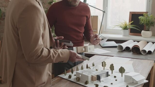 Tilt-down slowmo of professional male architects creating 3d layout of modern two-floor house working together in loft-style office