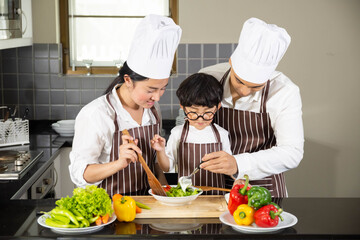 Asian woman young mother and father with son boy cooking salad food with vegetable holding tomatoes and carrots, bell peppers on plate for happy family cook food enjoyment lifestyle kitchen in home