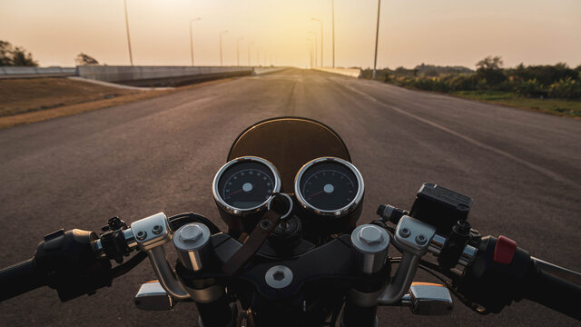 Driver riding motorcycle on an asphalt road in highway at sunset, details of the steering bar.
