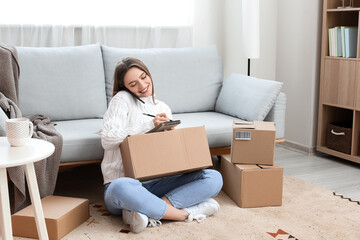 Young woman talking by mobile phone while preparing parcel for client at home