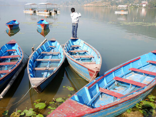 Fototapeta na wymiar Wooden canoe boat floating in Phewa Tal or Fewa Freshwater Lake wait service Nepali people and foreign travelers rowing travel relax visit tour at Gandaki Pradesh on December 7, 2017 in Pokhara, Nepal
