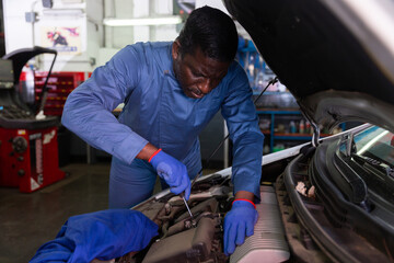 Fototapeta na wymiar African car mechanic with screwdriver repairing car engine under the hood in auto service