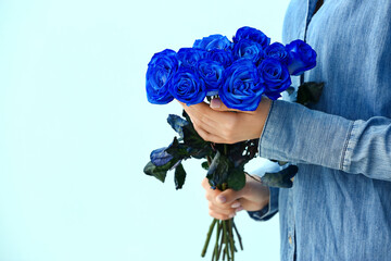 Woman with beautiful blue roses on color background