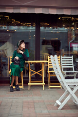 Happy woman in green dress in urban city is sitting near cafe