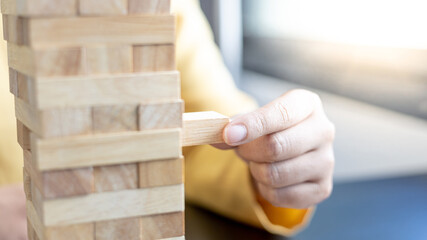 Business growth with wooden blocks concept, Planning to Reduce Investment Risks with Wooden Game Models, hand of a business woman placed a wooden block on a high tower,Management of limited resources.