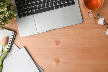 Laptop computer, notebook, cup and glasses on wooden desk.