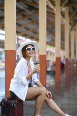 Cheerful young woman traveller awaiting the arrival of trains at railway station.