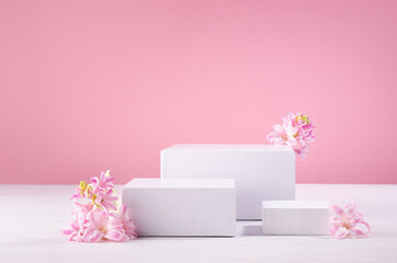 White rectangle podiums different size for presentation cosmetic produce or goods with fresh spring flowers and pastel pink background. Template for advertising.