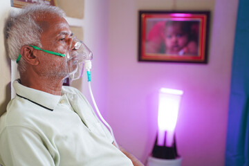 Old man with Oxygen concentrator mask reading news using mobile phone during home isolation -...
