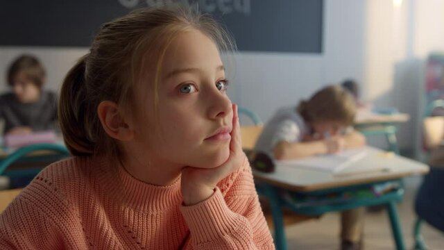 Dreamy kid sitting at desk in classroom. Thoughtful schoolgirl looking at window