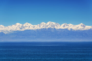 Big mountain lake Issyk-Kul, high snowy mountains, dark blue water, clear blue sky. Kyrgyzstan