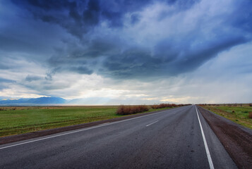 an asphalt road across the steppe of Kazakhstan in the direction of thunderclouds