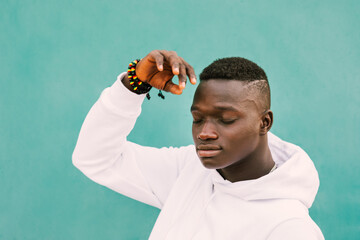 Portrait of young african black man with afro hair against a green wall wearing a white sweatshirt with his hand raised and eyes closed. Diversity and stop racism concept. BLM