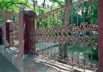 An old fence with decorative elements separating the courtyard from the street in an urban...