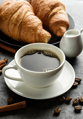 Close-up coffee cup with croissants and coffee beans.