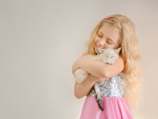 Little happy blonde girl hugs a beige sleeping kitten and smiles closing her eyes.