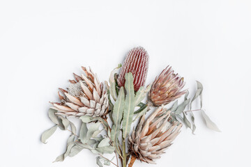 Beautiful dried flower bunch including Eucalyptus leaves,  King Protea and Banksia flowers in red, pink and purple on a white background, photographed from above.