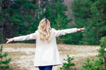 One young beautiful blonde long haired woman with raised hands over green natural forest background outdoor.