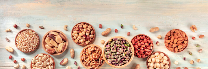 Nuts, in wooden bowls and scattered, shot from the top. Panoramic banner on a rustic background with copy space
