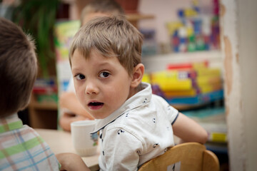 cute caucasian boy sitting at the table in kindergarden having breakfast.  Image with selective focus © Yulia Raneva