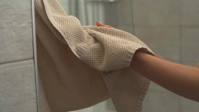 Close-up of unrecognizable young woman drying hands on towel in modern bathroom after washing arms with liquid soap sanitizer gel. Closeup of female wipes hands with towel. Shooting in slow motion.