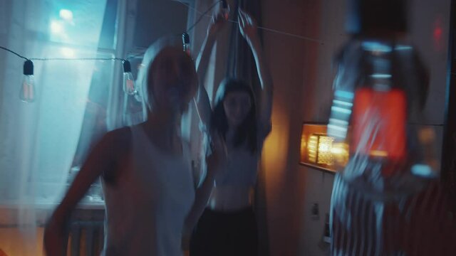 Company of young ecstatic girlfriends jumping, raising arms up and yelling in excitement while dancing at home retro party