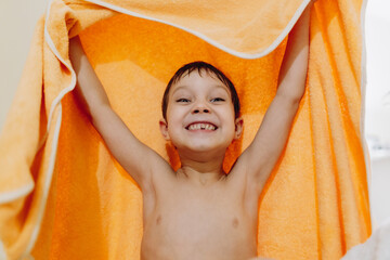 portrait of cute caucasian 6 year old boy with lost front tooth holding an orange towel, after...