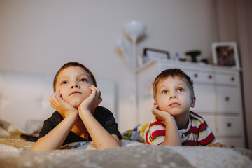 cute caucasian brothers lie in a bed watching cartoons on tv. Image with selective focus.