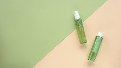 Two green cosmetic bottles with face washing gel and tonic on beige and green background. Natural organic cosmetics. Top view, flat lay