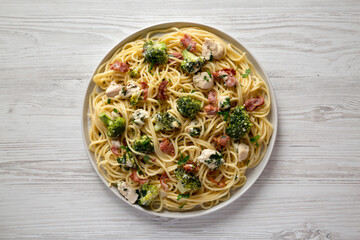 Homemade Chicken Bacon Broccoli Alfredo on a plate on a white wooden surface, top view. Flat lay, overhead, from above.