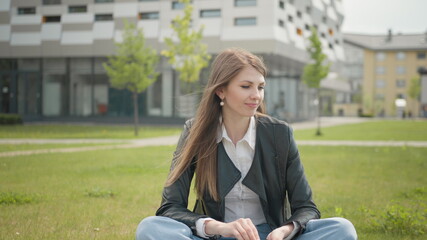 Attractive female student sitting on the grass near school or college or office. Teen woman,...