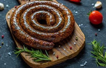 Grilled spiral sausages with garlic and seasoning on dark wooden background