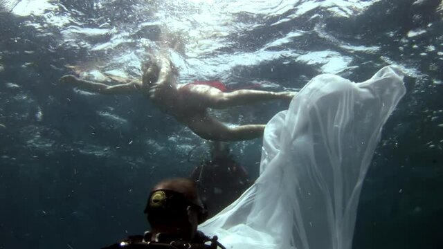 Young woman underwater model in white cloth on background of blue water. Concept of creativity and art of creating images.