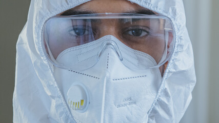 Portrait of male doctor nurse scientist medical worker wears special protective chemical white suit uniform goggles and respirator looking at camera with sad expression, fighting covid-19 pandemic
