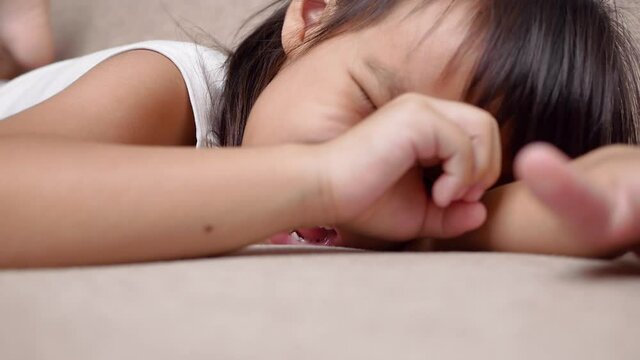 Cute little girl lying on sofa in the living room, looking at camera and smiling while playing at home.