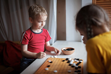Brother and sister playing Chinese chess go at home, sibling have fun together with igo go stones,...