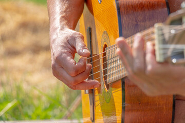 A man sits in the courtyard of a village house and plays an acoustic guitar. Close-up. Soft focus