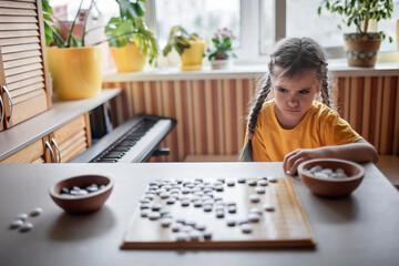 Sad girl looking at Chinese chess go board after game at home, she lost, igo go stones, without gadgets, traditional Chinese board game, digital detox, happy family moments